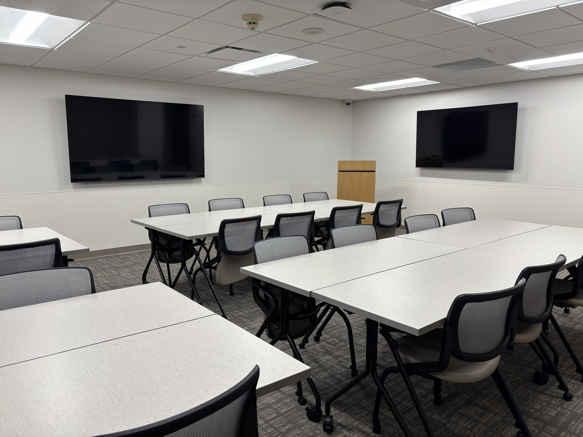 Tables, chairs, and two wall-mounted TVs in a training room within the YMCA Leadership Office