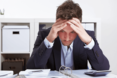 A stressed accountant who is holding his head in his hands looking at his financial pages.