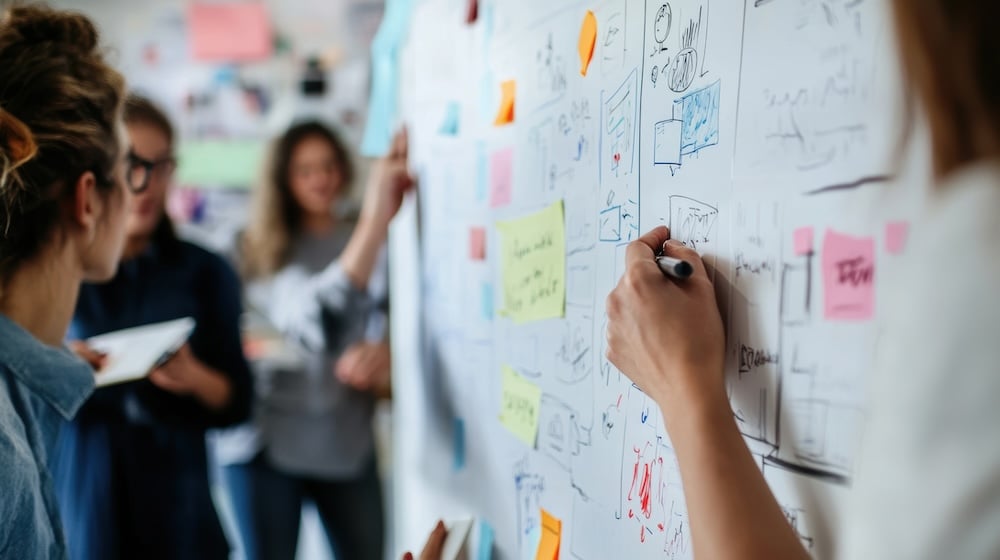 Business team collaborating on IT strategy and growth planning during a whiteboard brainstorming session focused on technology goals, workflow improvements, and long-term business planning.