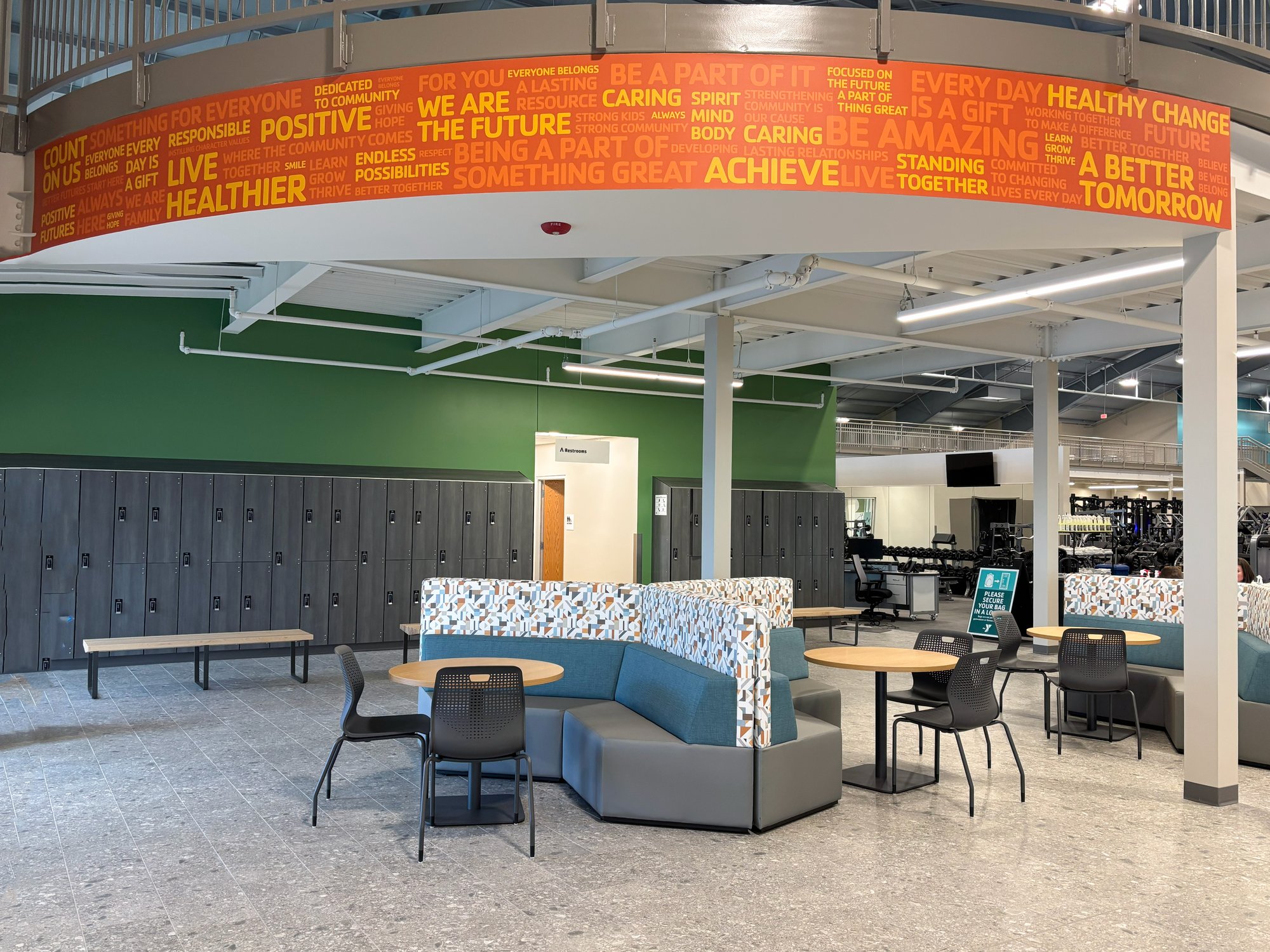 An orange mural is painted on a curved wall above a Tangram seating arrangement in grey, blue, and multi-color white. An orange mural is painted on a curved wall above a Tangram seating arrangement in grey, blue, and multi-color white.
