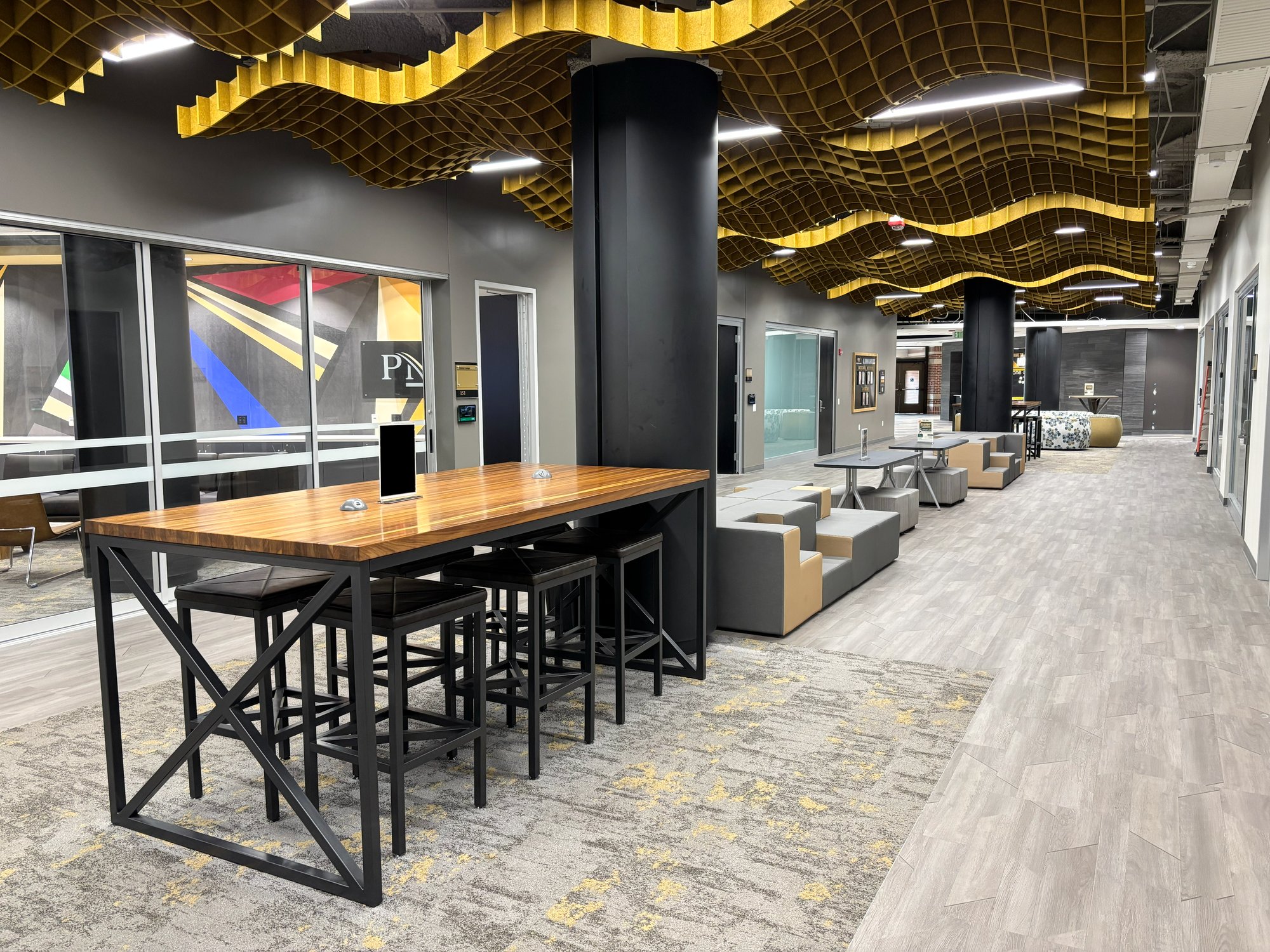 Long hallway with various tables and seating options with a gold waffle-textured noise dampener on the ceiling Long hallway with various tables and seating options with a gold waffle-textured noise dampener on the ceiling