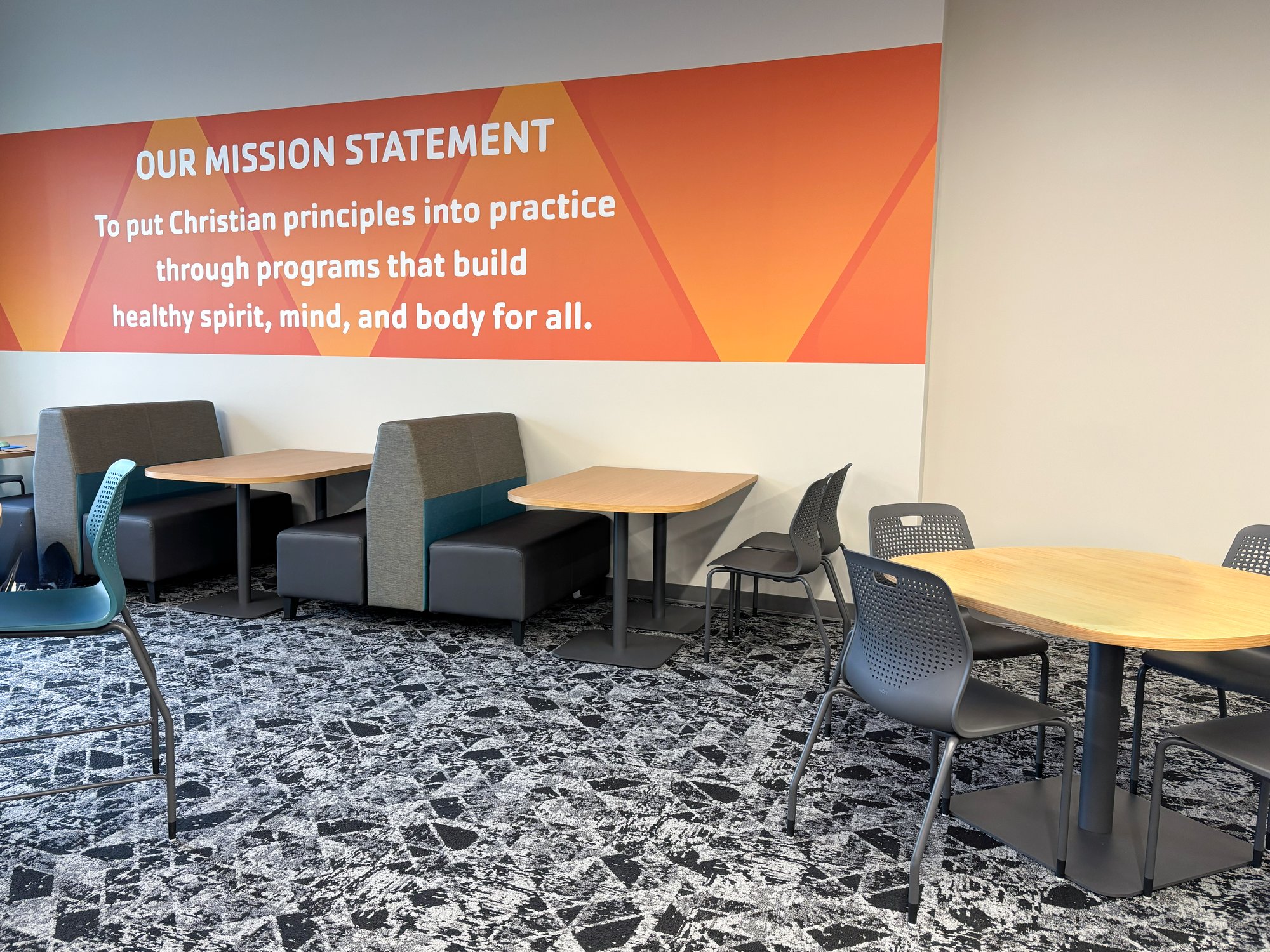 Booth and table seating sit in the lobby in front of the mission statement mural Booth and table seating sit in the lobby in front of the mission statement mural