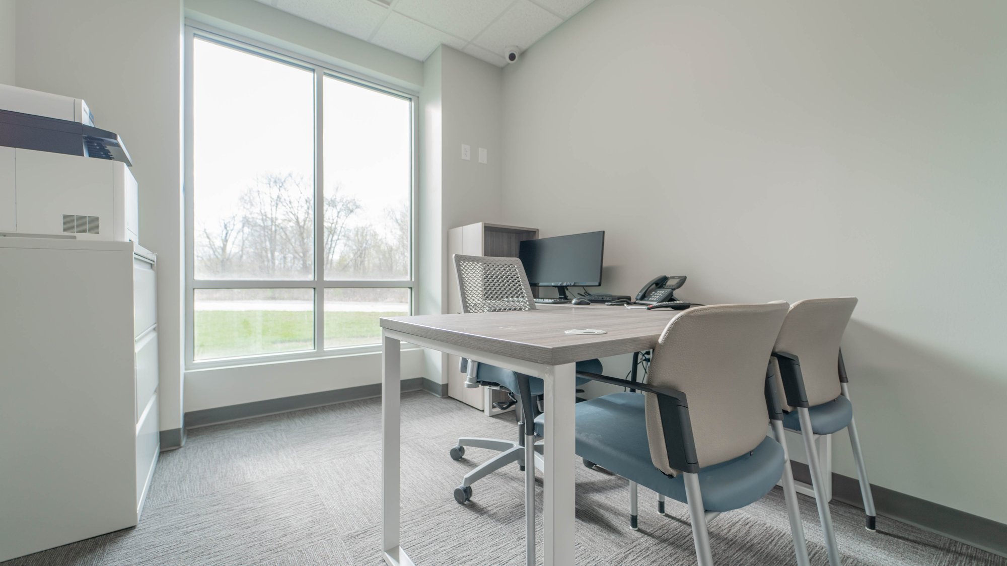 A desk with two chairs in front of a large window A desk with two chairs in front of a large window