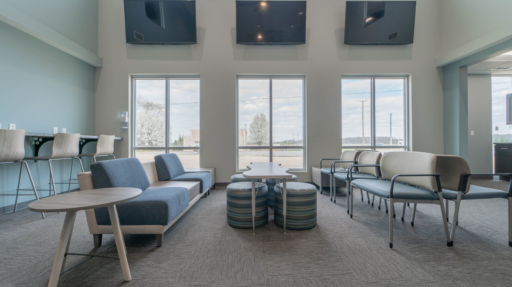 Three large windows with TVs hung over them backdrop seating areas in teal and grey color. Three large windows with TVs hung over them backdrop seating areas in teal and grey color.
