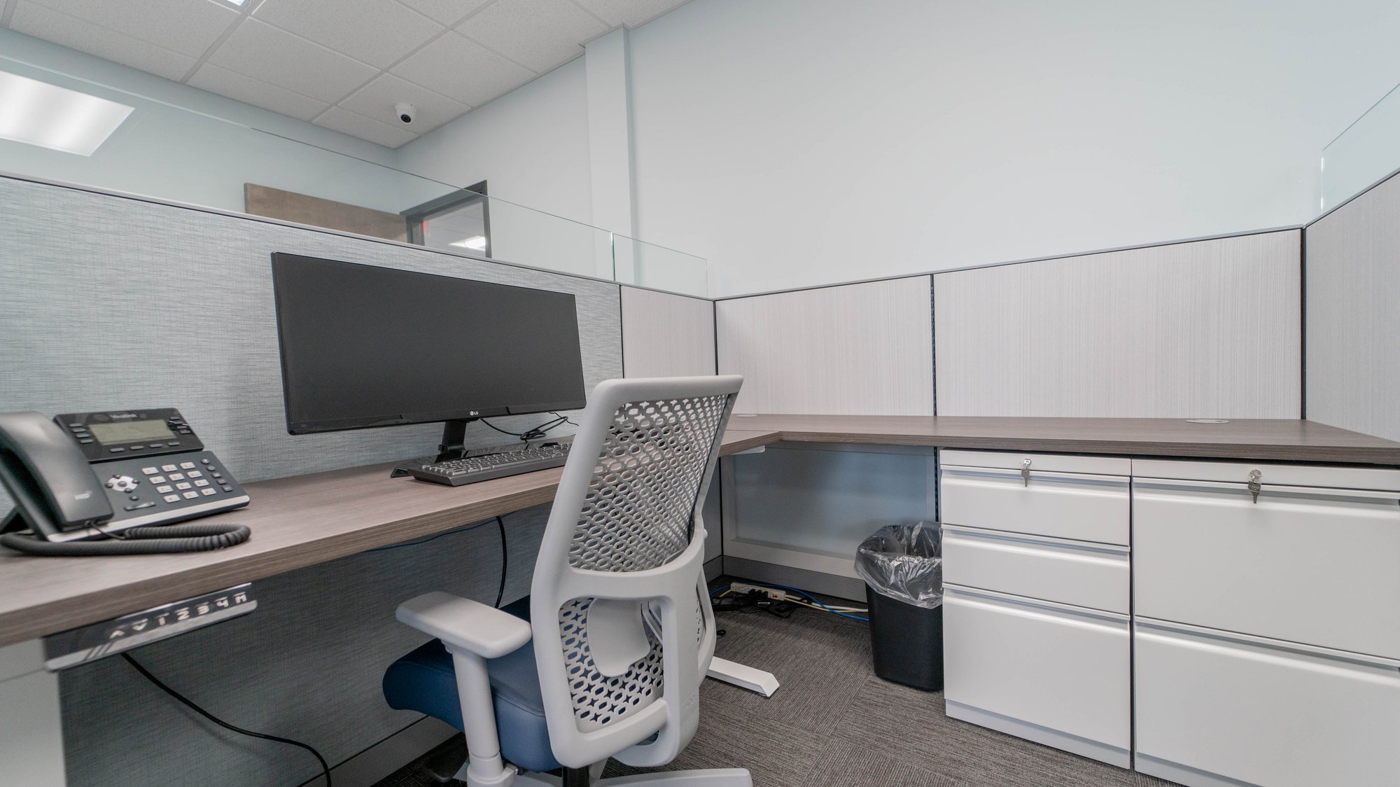 Cubicle space with sit-to-stand desk and blue-seated chair Cubicle space with sit-to-stand desk and blue-seated chair