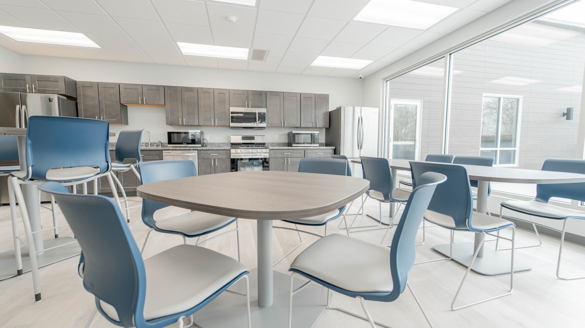 Kitchen area with many tables and blue chairs Kitchen area with many tables and blue chairs
