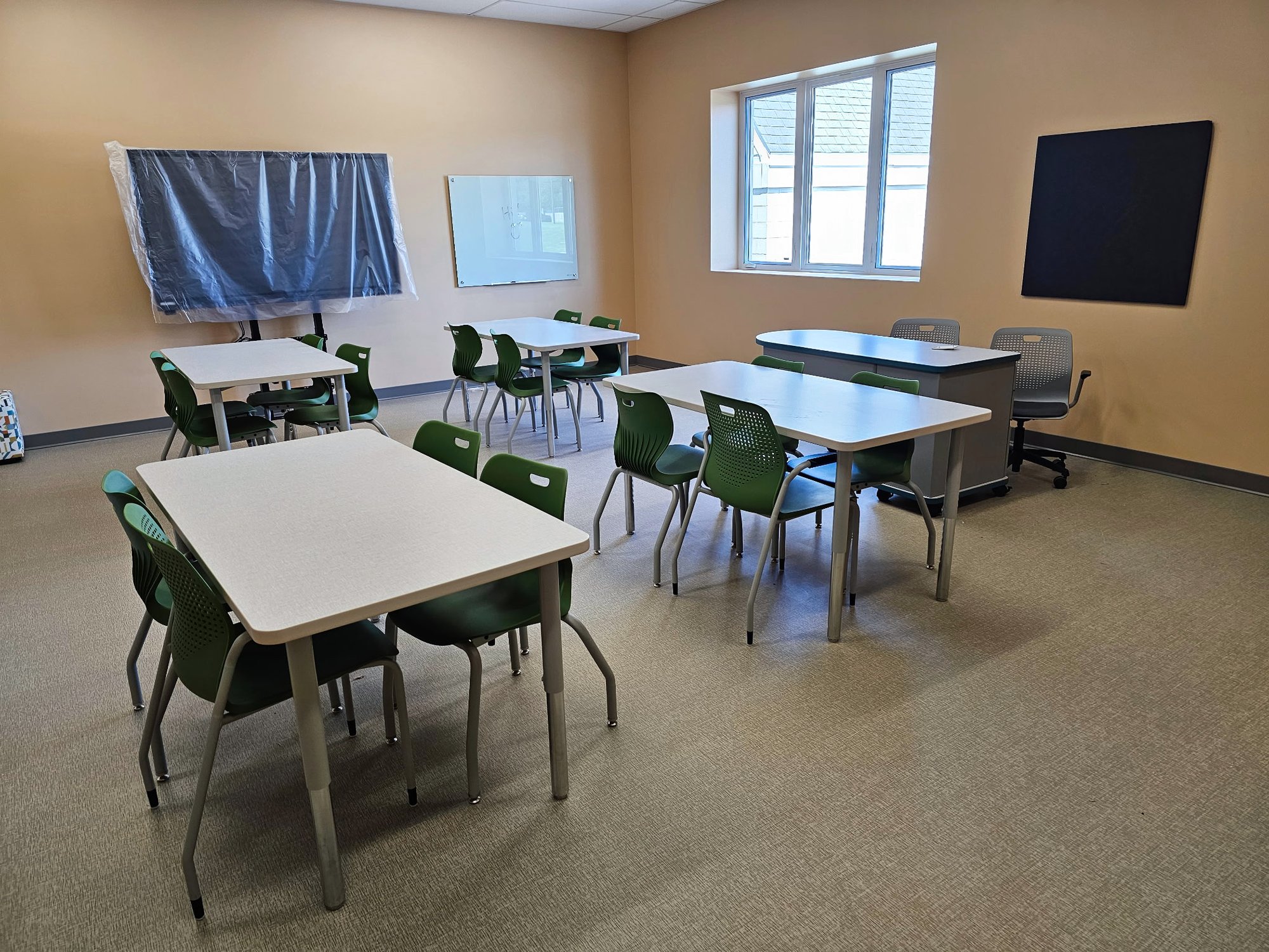 Four tables are arranged in a classroom with green chairs around them and a teacher's desk at the far wall Four tables are arranged in a classroom with green chairs around them and a teacher's desk at the far wall