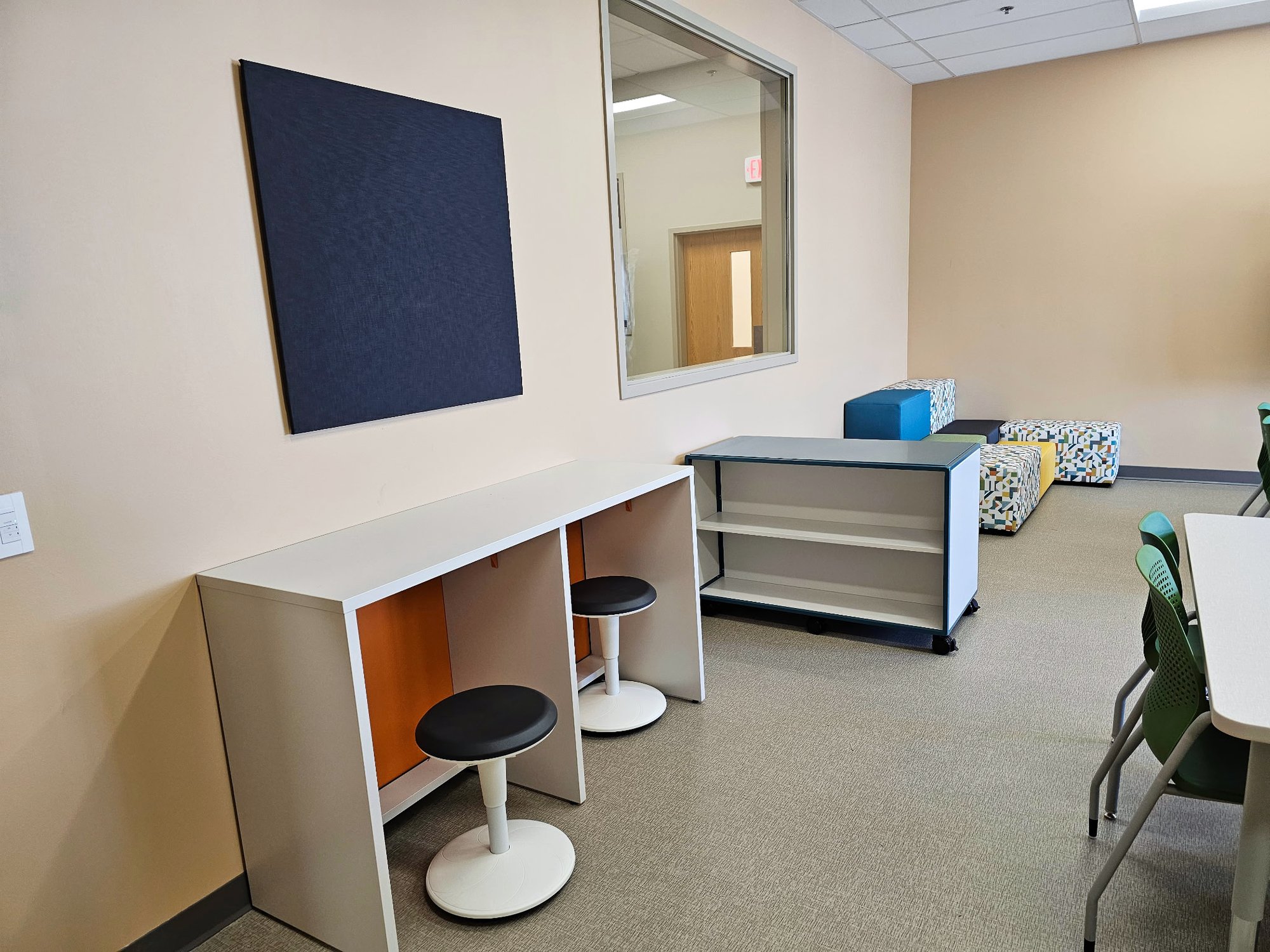 Stool sit under a cubby-esque counter in a classroom with multi-colored chairs and paneling. Stool sit under a cubby-esque counter in a classroom with multi-colored chairs and paneling.