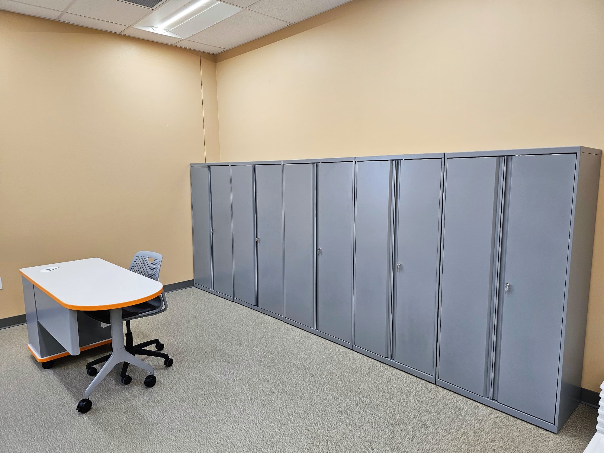 Storage lockers are lined up against the wall behind a desk with orange trim and a rolling chair Storage lockers are lined up against the wall behind a desk with orange trim and a rolling chair
