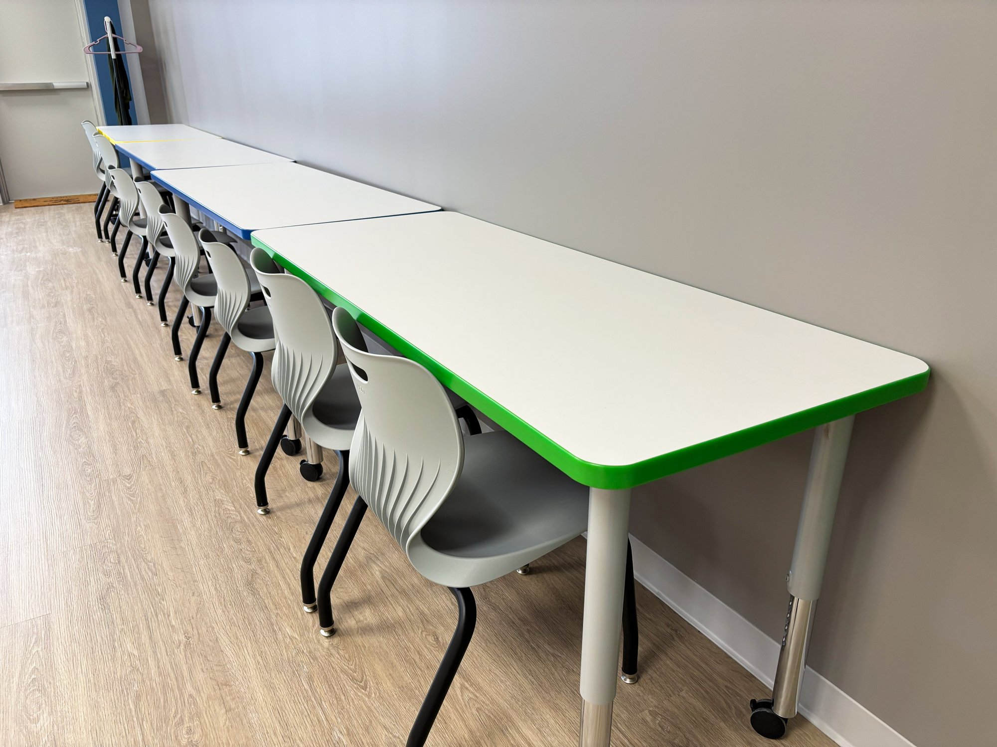 Tables with colorful edge banding are pushed against the wall, with chairs pushed in