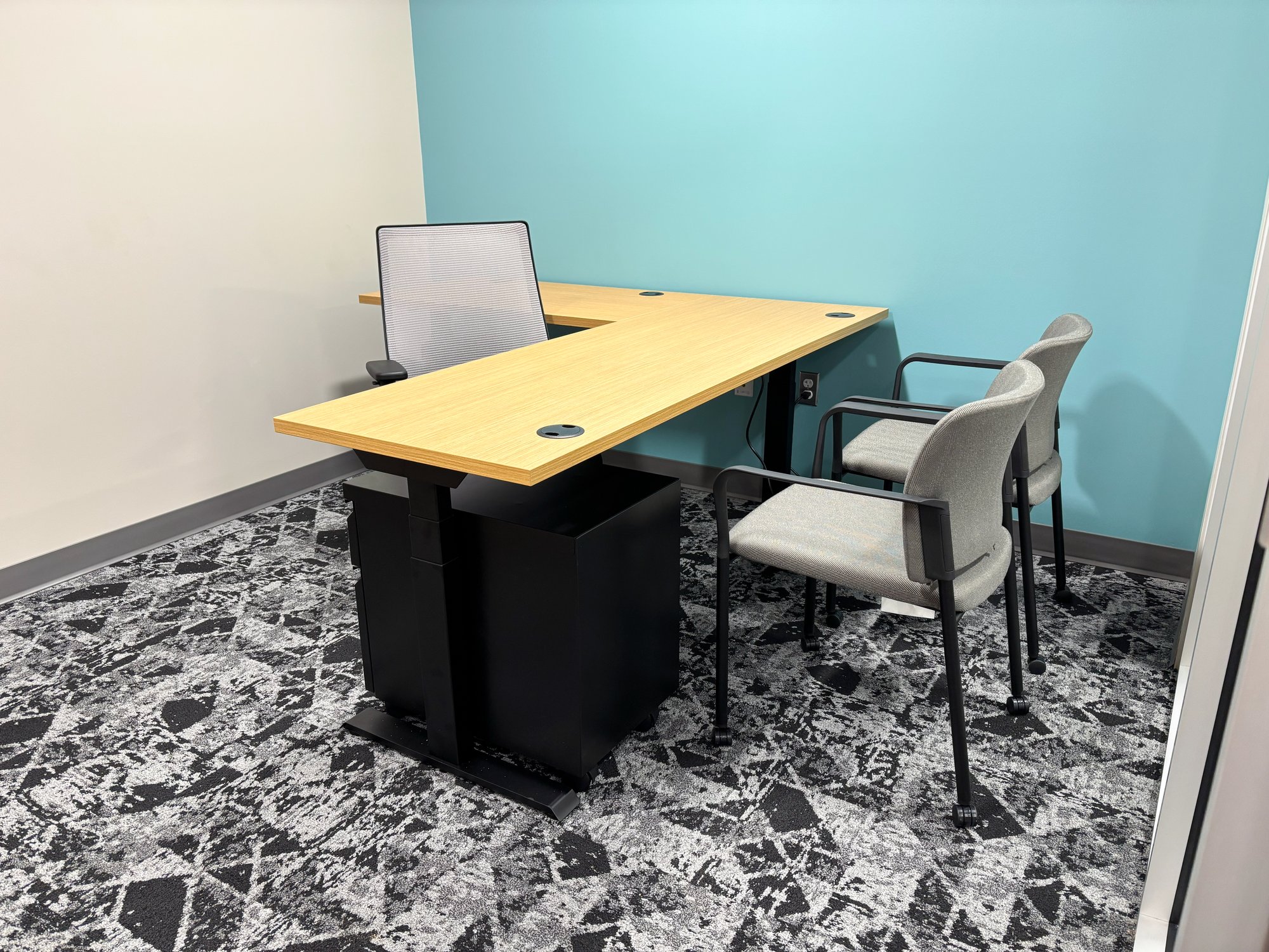 Personal office with a bright teal wall, grey chairs, and a height-adjustable desk Personal office with a bright teal wall, grey chairs, and a height-adjustable desk
