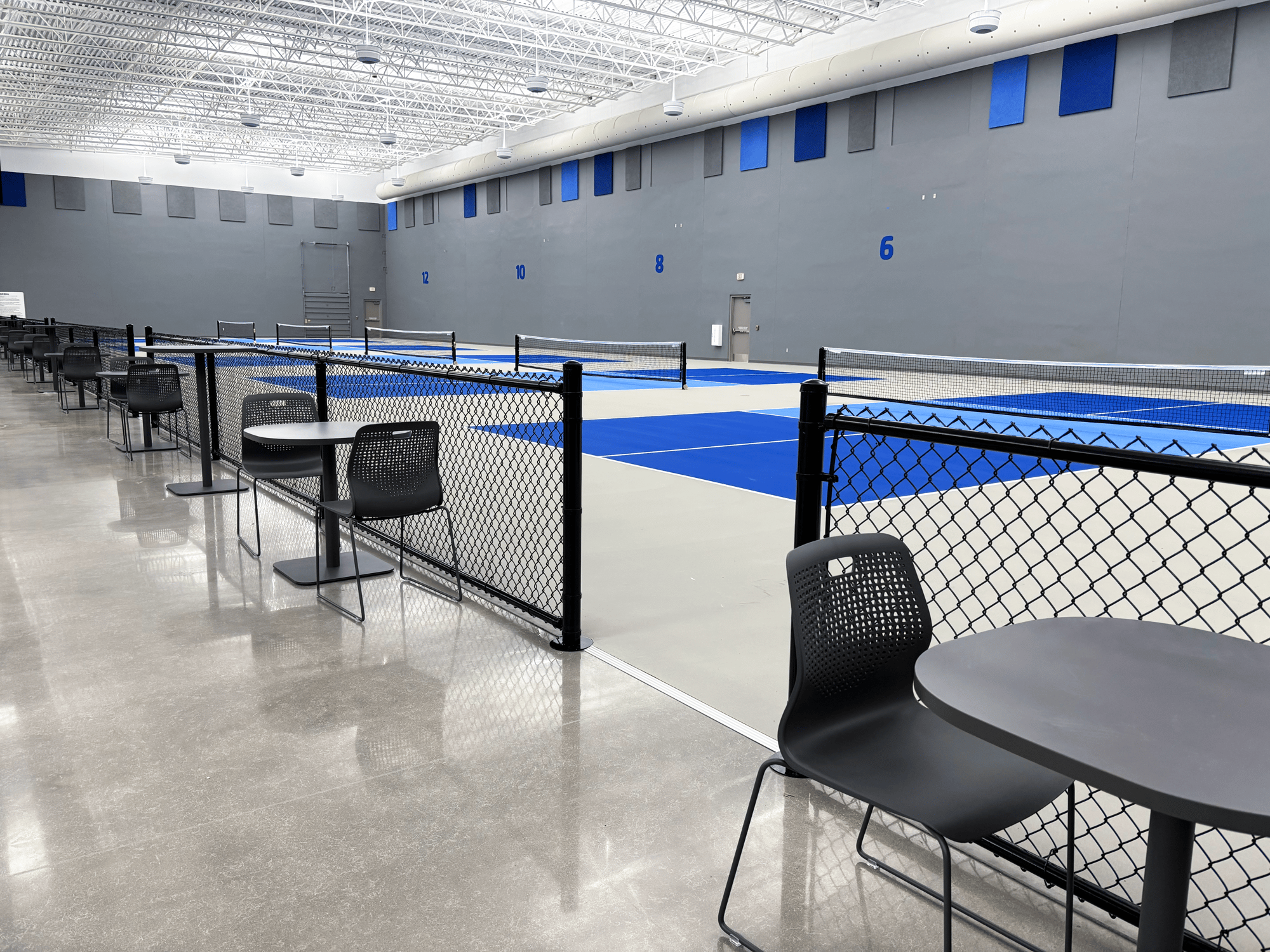 Five pickleball courts stand behind rows of tables and chairs next to chain-link fencing Five pickleball courts stand behind rows of tables and chairs next to chain-link fencing