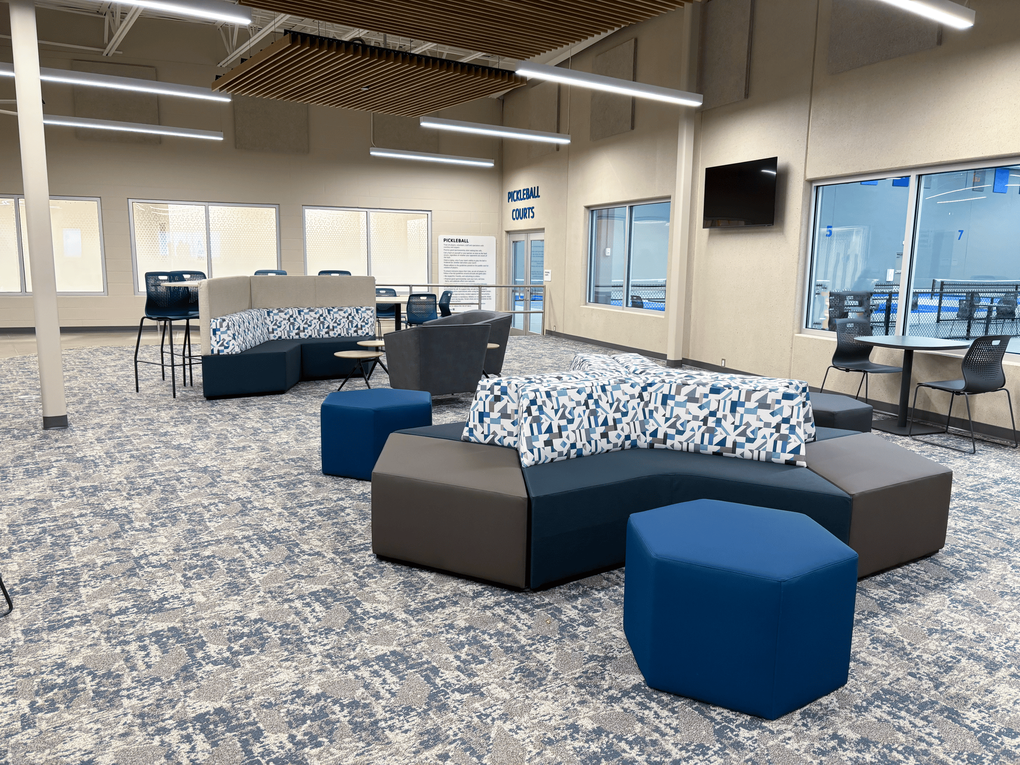 Angular couches and tables by large windows showing a pickleball court Angular couches and tables by large windows showing a pickleball court