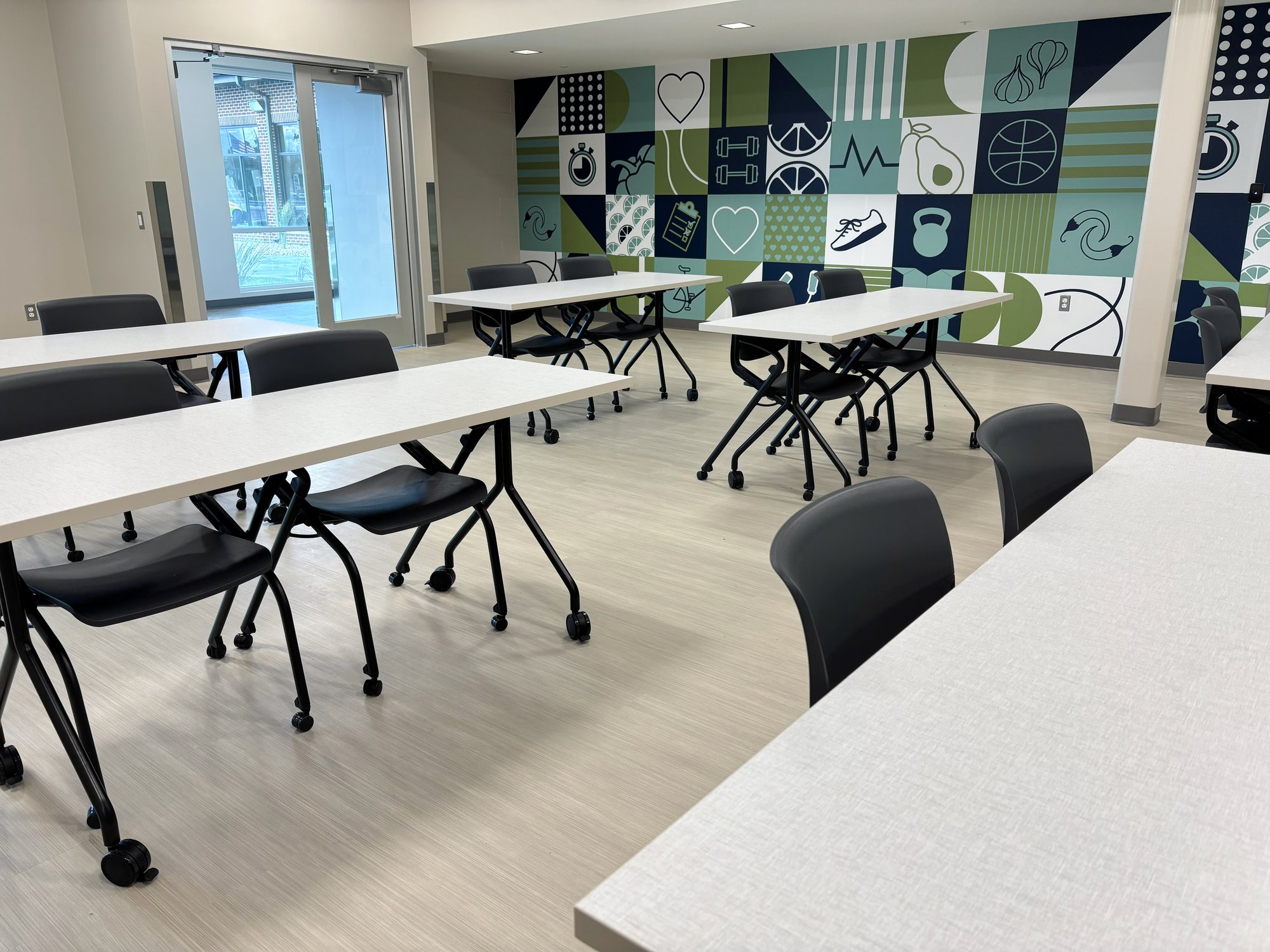 Tables and chairs in the teaching kitchen with a large mural on the wall Tables and chairs in the teaching kitchen with a large mural on the wall