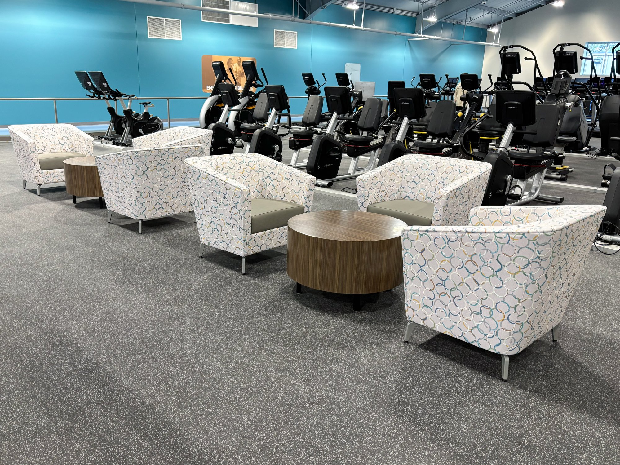 Multi-colored chairs in the upstairs lobby in front of rows of workout machines Multi-colored chairs in the upstairs lobby in front of rows of workout machines