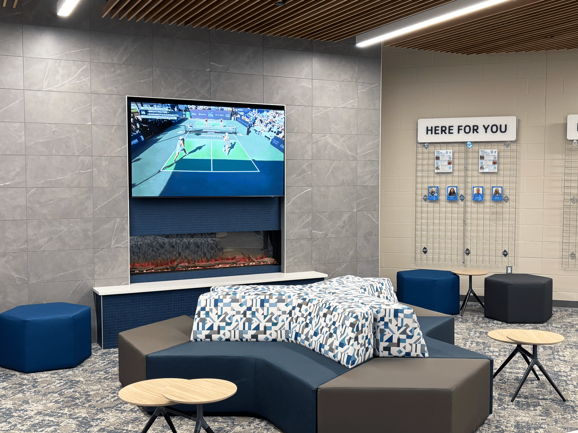 Angular couch seating by a faux fire and a TV showing a tennis game Angular couch seating by a faux fire and a TV showing a tennis game