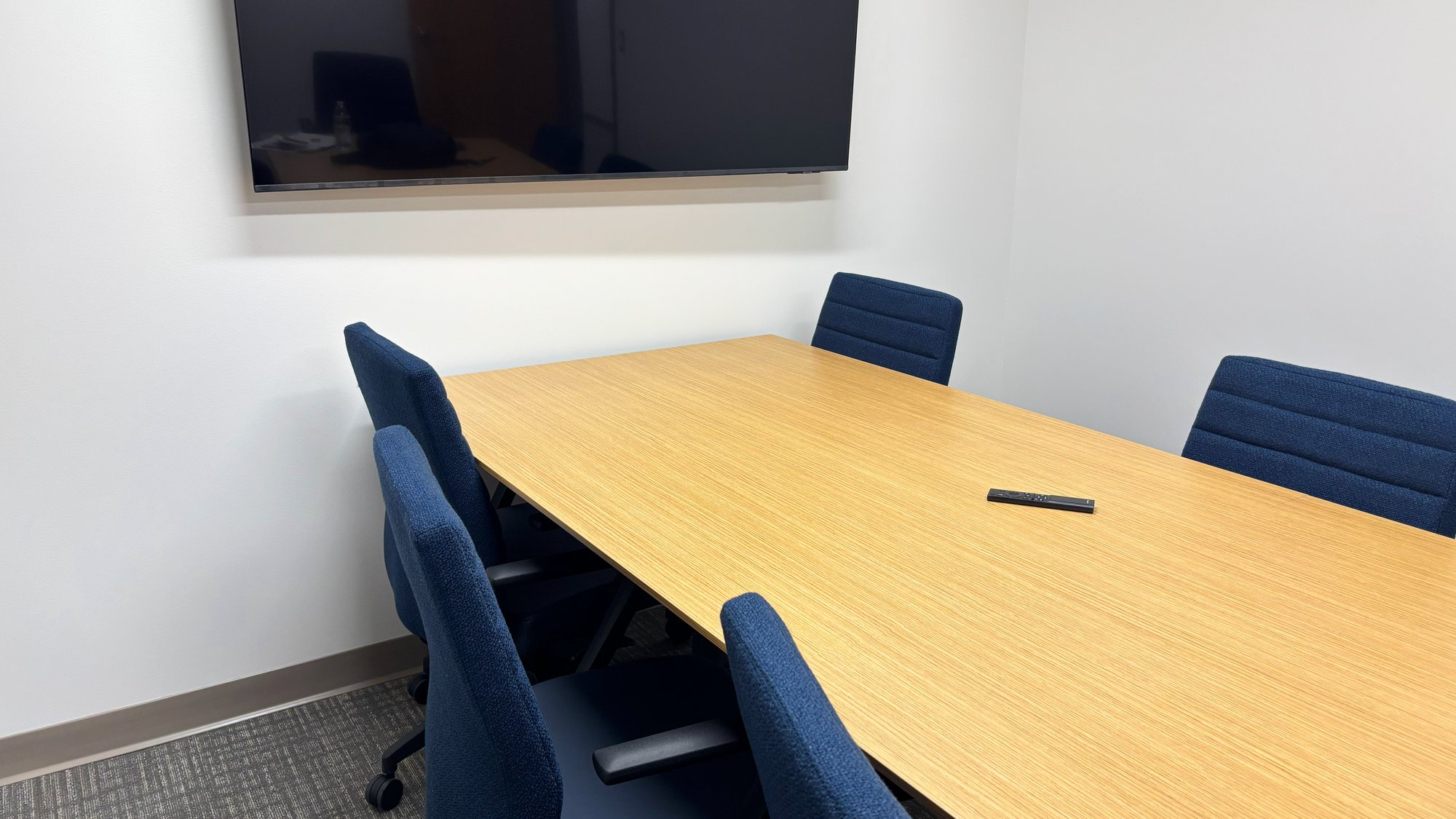 Conference room with a large table, blue rolling chairs, and a wall-mounted TV Conference room with a large table, blue rolling chairs, and a wall-mounted TV