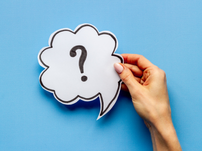 A light blue background with a hand holding a paper cut out of a talk bubble with a question mark.