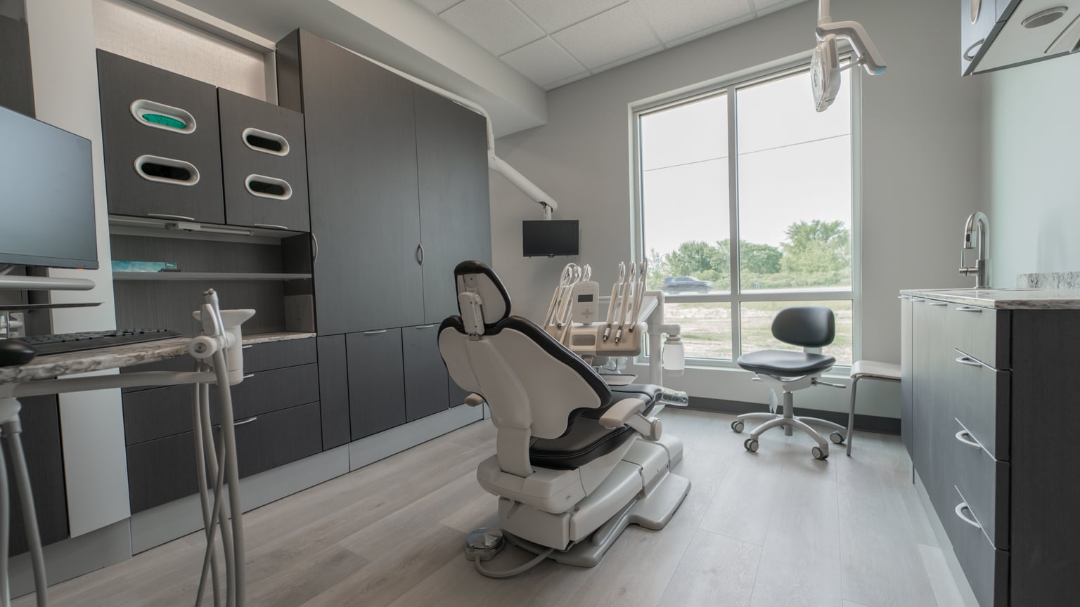 Examination room featuring a dentistry chair, a rolling chair, and various cabinet storage options