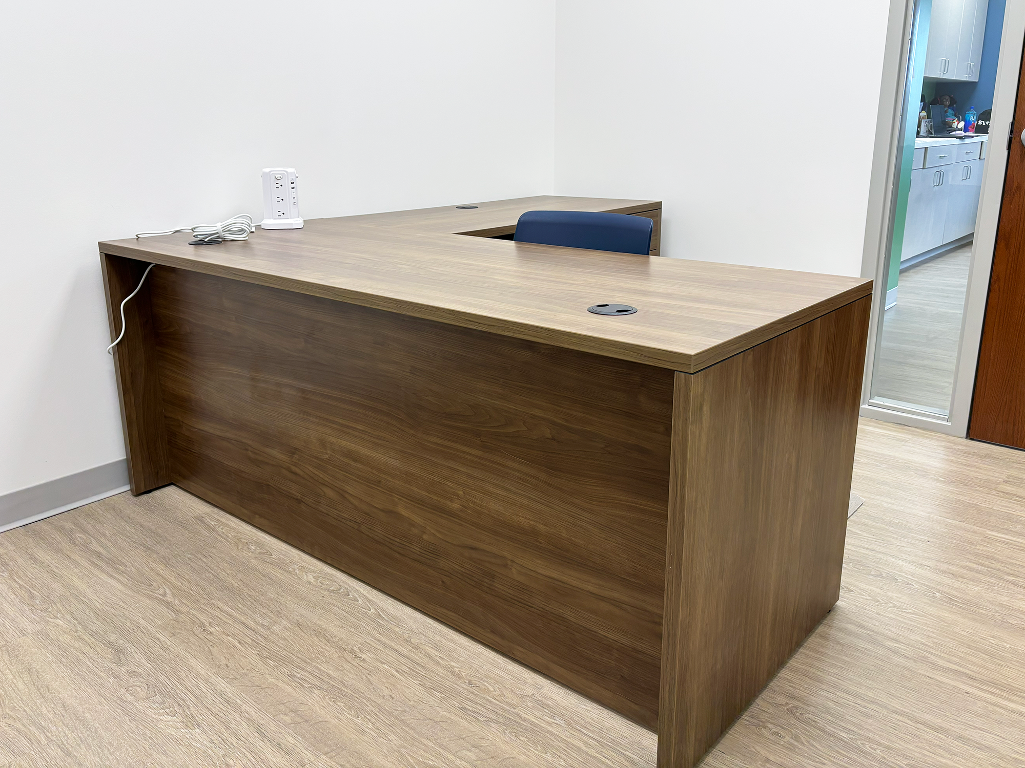 An empty desk sits in a small office with a navy blue chair behind the desk
